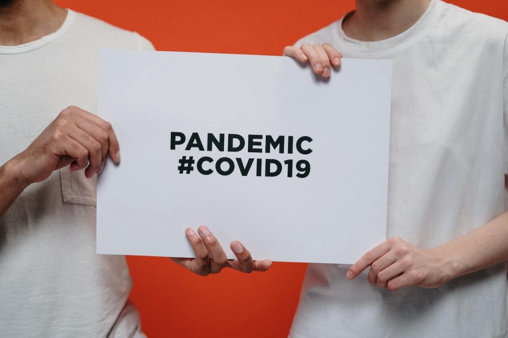Two people holding a sign that reads 'Pandemic #COVID,' symbolizing awareness and impact of the COVID-19 pandemic.